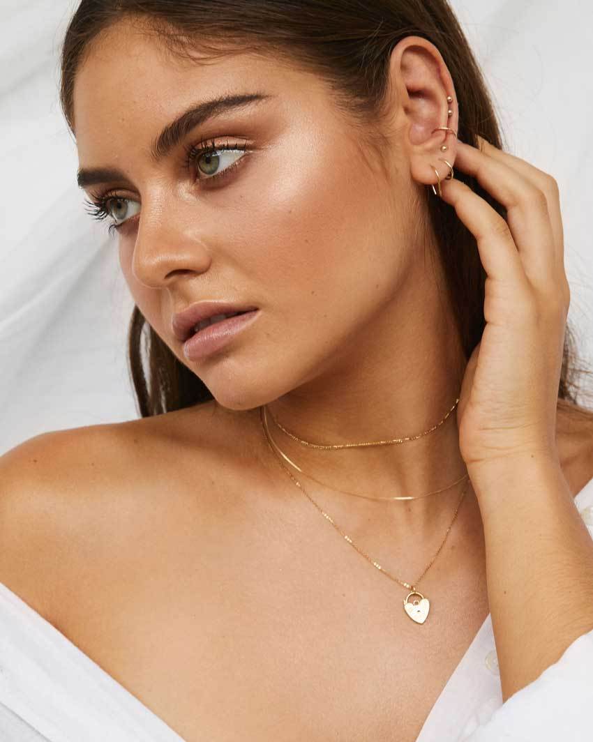 Model wears multiple earrings and layered gold necklaces