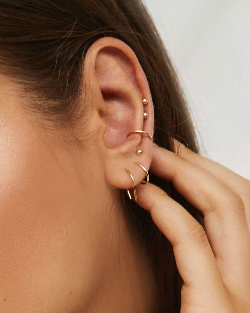Model wears arc earrings gold, hoops, studs and fine ear cuffs in multiple piercings